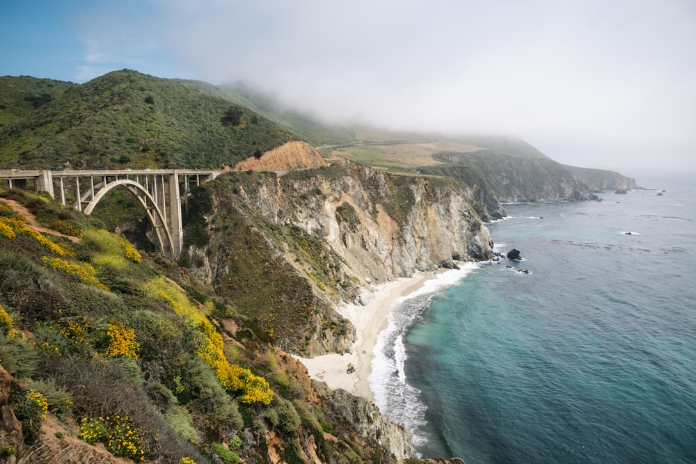 a bridge over a body of water next to a lush green hillside