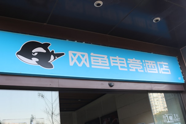 A building entrance features a vibrant blue sign with white Chinese characters and a stylized orca logo in black and white. The overall appearance suggests an establishment focused on eSports or digital activities.