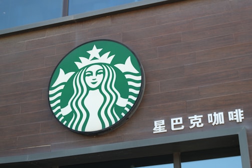 A circular logo featuring a stylized mermaid with two tails, placed on a dark brown wooden wall. To the right, there are Chinese characters in white.