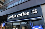 A modern storefront features the sign 'luckin coffee' in bold, white letters on a black background. The sign also includes Chinese characters next to it. The facade of the building is sleek and urban with floor-to-ceiling windows on the upper floors.