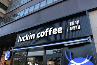A modern storefront features the sign 'luckin coffee' in bold, white letters on a black background. The sign also includes Chinese characters next to it. The facade of the building is sleek and urban with floor-to-ceiling windows on the upper floors.