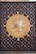 An ornate door features a prominent circular design in the center, with intricate Arabic calligraphy surrounded by geometric patterns. The wood is rich and dark, with metal accents and a golden-hued centerpiece showcasing elaborate detailing.