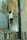 A person standing on a metal ladder, painting a mural on a wall. The mural depicts a large compass with text and a cloak draped over it. The room appears worn, with peeling paint and visible graffiti. Paint cans and a plastic bag are on the floor.