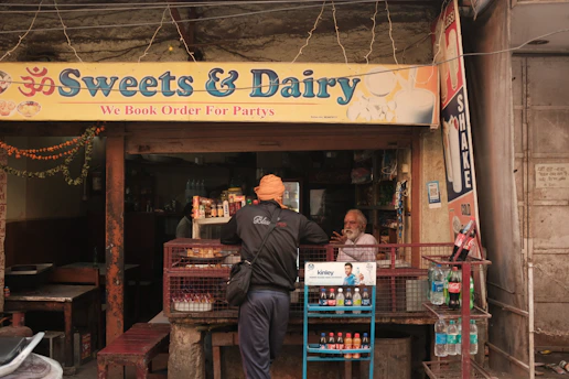 A smiling shopkeeper arranging Amul dairy products on shelves inside a kirana store.