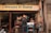 A small shop with a sign reading 'Sweets & Dairy' offers various beverages and snacks. A person with a turban is seen interacting with the shopkeeper, who is seated behind the counter. The shop is adorned with colorful decorations and is set in an urban environment.