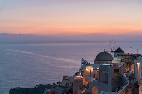 A serene Greek island coastline at sunset with whitewashed buildings and turquoise waters.