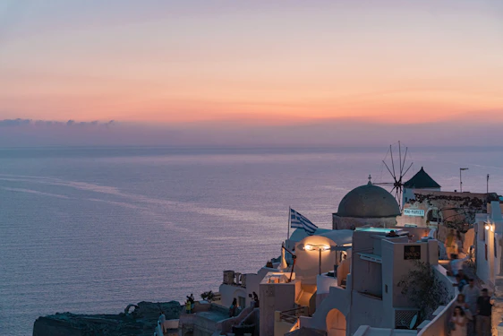 A serene coastal view of a modern Greek villa overlooking the Aegean Sea at sunset.