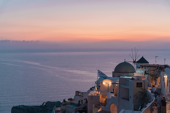 A serene Greek coastal village at sunset, with whitewashed buildings and blue domes.