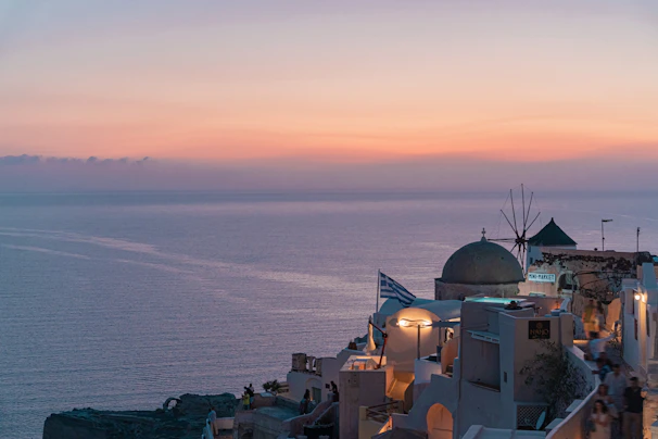 A serene Greek island sunset over calm waters, with greenery and a small village silhouetted.