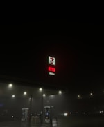 A dimly lit gas station at night with a visible 7-Eleven logo and a price display for diesel reading 279.9. The surroundings are dark, with only a few streetlights illuminating the scene.