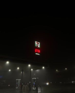 A dimly lit gas station at night with a visible 7-Eleven logo and a price display for diesel reading 279.9. The surroundings are dark, with only a few streetlights illuminating the scene.