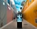 A walkway between two high-fashion branded walls with large advertisements for Tiffany & Co. and Fendi. A digital directory board displaying a fashion advertisement for Dior is placed in the center. A person carrying a shopping bag walks along the path. The sky above is bright with scattered clouds.
