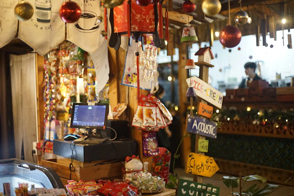 A warm, cozy shop counter with softly glowing candles and delicate religious gifts displayed beside a cheerful welcome sign.