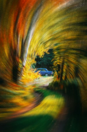 A vivid swirl of autumn colors frames a classic car parked in a natural setting, creating a dynamic and artistic effect.