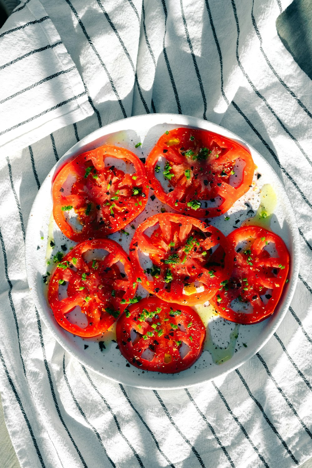 um prato branco coberto com tomates fatiados em cima de uma mesa