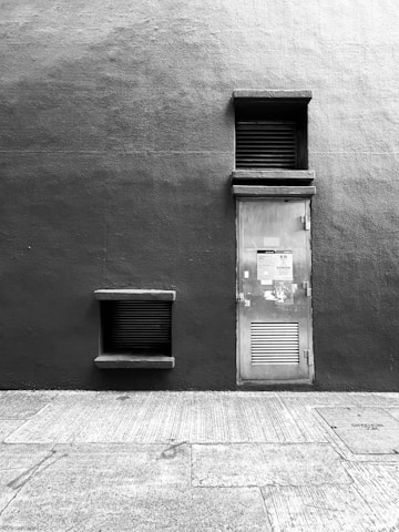 A contemplative black-and-white street scene from Singapore, showing a weathered wall reflecting soft light, embodying stillness and depth.