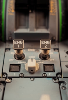 Close-up view of an aircraft cockpit dashboard, focusing on engine controls labeled 'ENG 1' and 'ENG 2'. The image captures various switches and dials, including labels for crank, start, and off positions.
