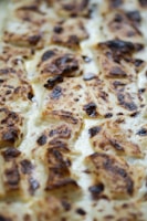 A close-up view of a baked dish with perfectly browned, crispy edges and a creamy texture. The surface appears to have caramelized spots, suggesting cheese or cream was used in the preparation.