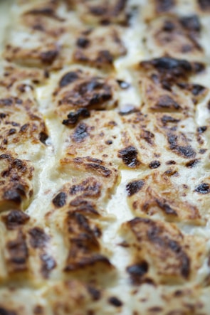 A close-up view of a baked dish with perfectly browned, crispy edges and a creamy texture. The surface appears to have caramelized spots, suggesting cheese or cream was used in the preparation.