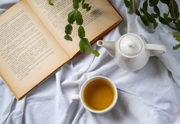 A serene morning scene with a steaming cup of herbal tea and an open book by a sunlit window, surrounded by green plants.