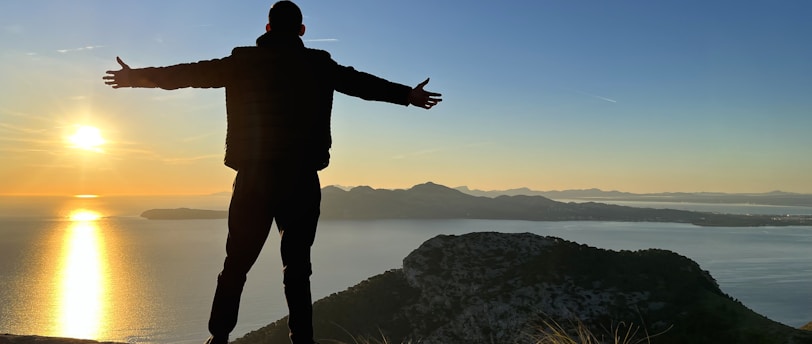 a man standing on top of a cliff next to a body of water