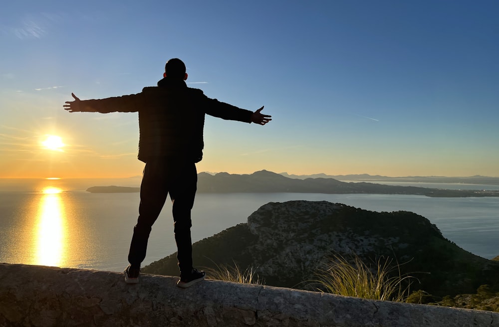 Un hombre parado en la cima de un acantilado junto a un cuerpo de agua