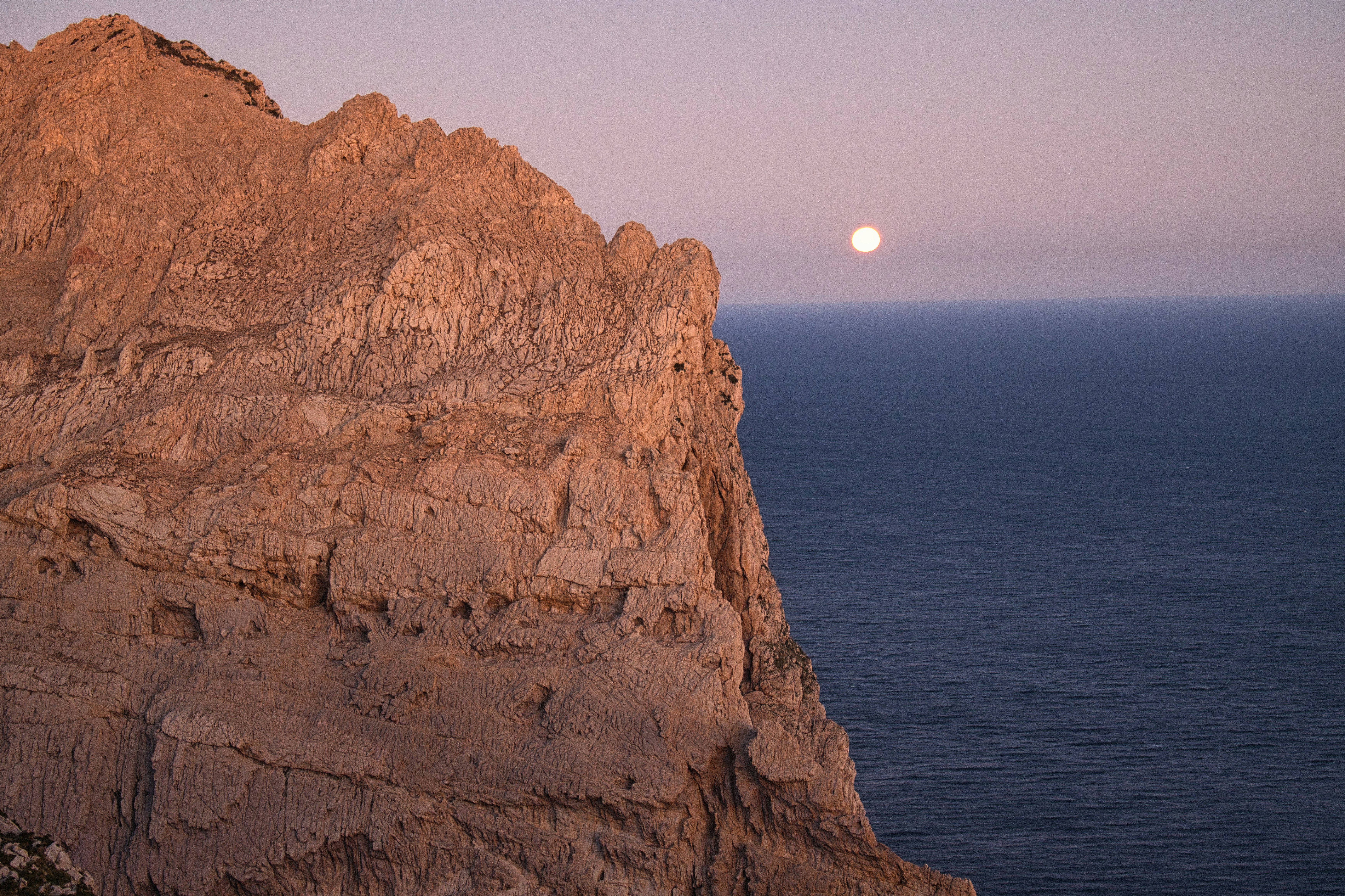 a full moon rising over the ocean from a rocky cliff, 