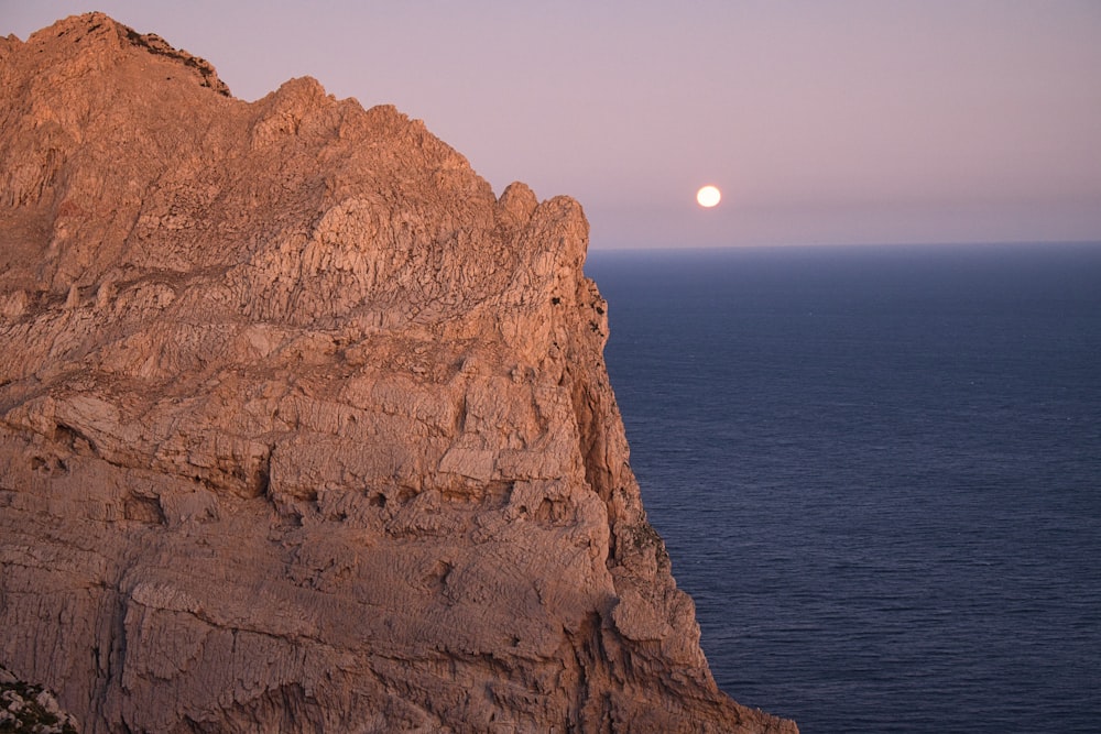 a full moon rising over the ocean from a rocky cliff