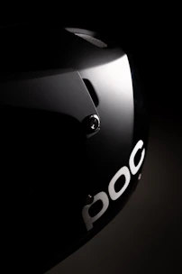 A glossy black helmet with red stripes, placed on a reflective surface under moody lighting.