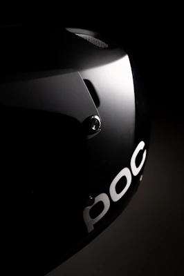 A glossy black helmet with red stripes, placed on a reflective surface under moody lighting.