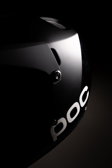 A sleek black helmet is partially illuminated, highlighting its smooth surface and the letters 
