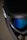 A close-up view of a ski or snowboard goggle with a black frame and blue reflective lenses. The strap is visible, as well as part of the goggle’s branding, which reads 'ORA'. The background is blurred, bringing focus to the goggles.