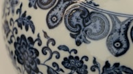 Detailed blue floral and abstract patterns are intricately designed on the surface of a ceramic object, likely porcelain. The patterns include swirling vines and floral motifs.