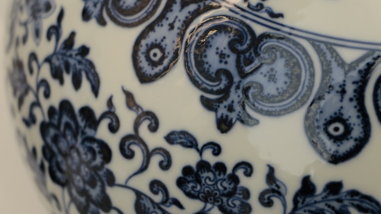 Detailed blue floral and abstract patterns are intricately designed on the surface of a ceramic object, likely porcelain. The patterns include swirling vines and floral motifs.