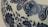 Detailed blue floral and abstract patterns are intricately designed on the surface of a ceramic object, likely porcelain. The patterns include swirling vines and floral motifs.