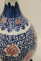 A detailed ceramic vase featuring intricate blue floral and vine patterns, accented with pink flower motifs. The craftsmanship showcases a blend of traditional design components, combining organic shapes with ornate detailing.