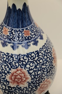 A detailed ceramic vase featuring intricate blue floral and vine patterns, accented with pink flower motifs. The craftsmanship showcases a blend of traditional design components, combining organic shapes with ornate detailing.