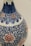 A detailed ceramic vase featuring intricate blue floral and vine patterns, accented with pink flower motifs. The craftsmanship showcases a blend of traditional design components, combining organic shapes with ornate detailing.