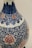 A detailed ceramic vase featuring intricate blue floral and vine patterns, accented with pink flower motifs. The craftsmanship showcases a blend of traditional design components, combining organic shapes with ornate detailing.