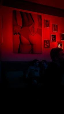 Cozy corner of a gallery with plush seating and red lighting highlighting abstract paintings.
