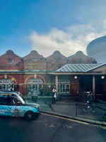 A vialuxe taxi parked near a vibrant event venue in Birmingham, ready for passengers.