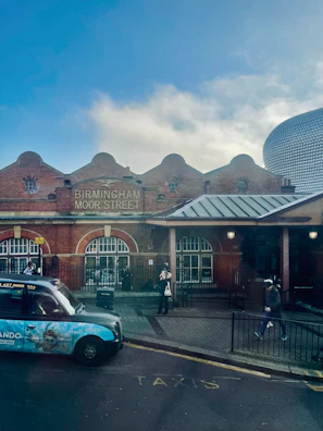 A vialuxe taxi parked near a vibrant event venue in Birmingham, ready for passengers.