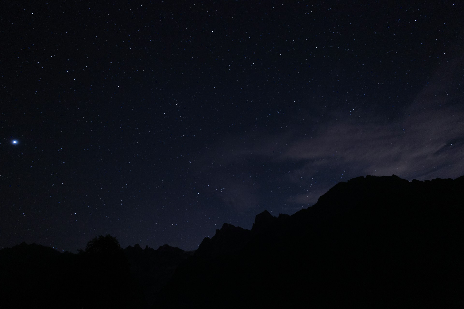 the night sky with stars above a mountain range