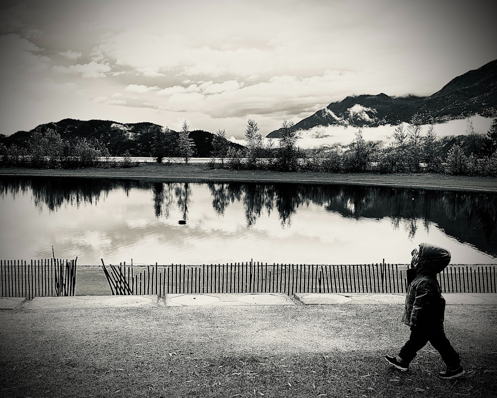 a person walking past a lake with mountains in the background