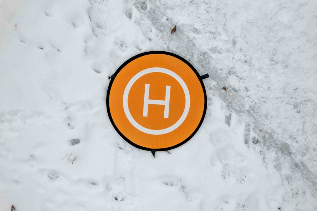 a sign that is on the ground in the snow, A bright orange helicopter landing pad sign with the letter
