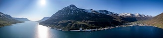 A panoramic view of Greenland’s rugged coastline with mining sites and fishing boats under a clear sky.