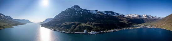 A panoramic view of Greenland’s rugged coastline with mining sites and fishing boats under a clear sky.