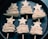 Six pastry pieces shaped like stylized Christmas trees are arranged in rows on a dark baking tray. Each piece comprises layered pastry folded in a zig-zag pattern, topped with a star and held together by a skewer.