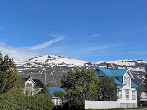 View of the renovated tourist house nestled among green mountain trees with a vivid blue sky.