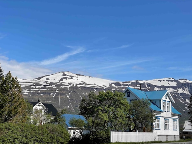 View of the renovated tourist house nestled among green mountain trees with a vivid blue sky.